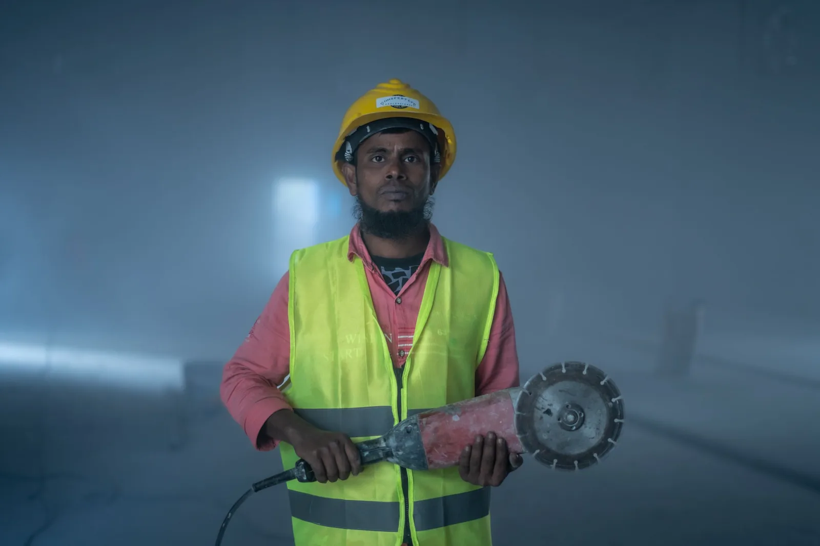 A site worker in a hard hat and high-visibility vest holding a concrete saw
